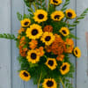 Sunflower and orange floral arrangement with greenery against a blue wood background