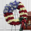 Circular wreath of red and cream roses with blue flowers on a stand