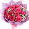 Bouquet of bright pink roses with white filler flowers wrapped in purple paper