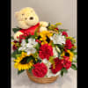 Basket arrangement with a teddy bear and mixed red, yellow, and white flowers