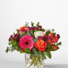 Mixed bouquet of pink, orange, and white flowers in a clear glass vase