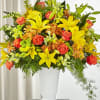 Bright mixed bouquet of yellow lilies, orange roses, and daisies in a white vase