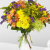 Mixed bouquet of yellow, purple, and peach flowers in a clear glass vase