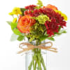 Orange roses and red chrysanthemums in a clear glass vase with a raffia bow