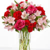 Pink roses, red carnations, and pale pink alstroemeria in a clear glass vase