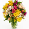 Mixed bouquet of yellow, pink, and white flowers in a clear glass vase