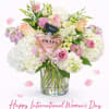 Pink and white flower arrangement in a glass vase with a Prada perfume bottle