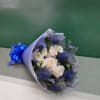 Bouquet of pale roses, white blooms, and blue thistle wrapped in lavender paper