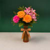 Orange roses and pink alstroemeria in an amber vase with a ribbon