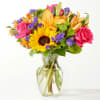 Mixed bouquet of sunflowers, roses, and lilies in a clear glass vase