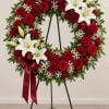 Red rose and white lily wreath on a stand with a burgundy ribbon