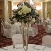 Tall white floral centerpiece in a clear glass vase on a banquet table