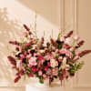 Large pink and burgundy floral arrangement in a white pedestal vase