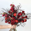 Handheld bouquet of red roses and red blooms with dark foliage