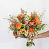 Handheld bouquet of orange, yellow, and pink flowers with airy greenery