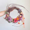 Handheld floral wreath with purple, pink, and orange blooms on a twig frame