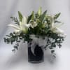 White lilies arranged in a dark vase with a sheer silver bow