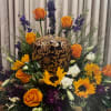 Orange roses and yellow sunflowers arranged around an ornate black-and-gold urn.