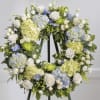 Floral wreath with white roses, blue hydrangeas, and pale green blooms on an easel