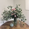 Pink spray roses in a green glass vase with large eucalyptus branches
