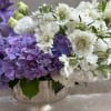 Purple and white floral arrangement in a decorative bowl vase