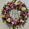 Heart-shaped floral wreath with pink, purple, yellow, and white blooms on a black stand
