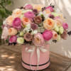Pink and peach roses arranged in a round pink box with a ribbon