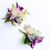 Two purple and white floral boutonnieres with ribbon on a white background