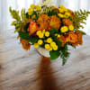 Orange and yellow floral arrangement in a white vase with a birthday topper