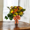 Bouquet of yellow and orange flowers in a glass vase with a patterned ribbon