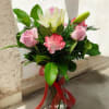 Pink roses and a white lily in a glass vase with a red ribbon