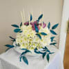 White chrysanthemum arrangement with purple roses and tall candles in a white bowl