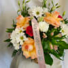 Peach roses and white daisies in a basket with a pink ribbon