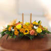 Low floral centerpiece with yellow roses, orange mums, and candles
