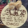 Round hanging sign with three puppy illustrations and the words "No need to knock, we're here (dogs)"