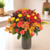 Mixed autumn bouquet in a textured glass vase with red, orange, and yellow blooms