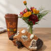 Fall-themed cup beside a small flower arrangement and folded blanket