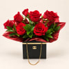 Red roses arranged in a black gift box with gold chain handles