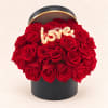 Red roses arranged in a black round box with a lit "love" topper