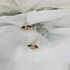 Pair of bee-shaped drop earrings on white fabric with faux greenery