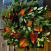 Holiday wreath with evergreen branches, red berries, and orange leaves