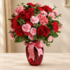 Red roses and pink carnations in a red glass vase with a pink ribbon