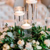 White roses and greenery surround three glass candle cylinders