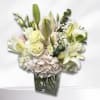 White lilies and roses arranged in a clear glass vase with pale hydrangea