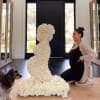 Large white rose floral sculpture beside a kneeling pregnant woman and a small dog