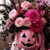 Pink floral arrangement in a jack-o'-lantern container with a small ghost figurine