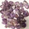 Pile of polished purple amethyst stones on a white surface
