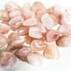 Pile of polished pink and peach tumbled stones on a white surface