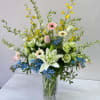 Mixed bouquet in a clear glass vase with lilies, gerberas, and blue flowers