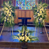 Large white floral arrangements flank a church podium with a smaller matching arrangement in front.